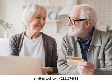 Happy Old Senior Elderly Caucasian Couple Grandparents Husband And Wife Paying Domestic Bills, Doing Online Shopping With Credit Card And Laptop, E-banking And E-commerce At Home