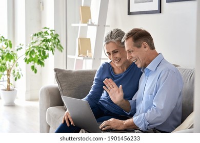 Happy Old Senior Grandparents Couple Waving Hand Making Online Video Call Enjoying Family Virtual Meeting Digital Webcam Videocall Chat Talking, Looking At Laptop Computer Sitting On Couch At Home.