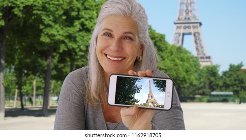 Happy Old White Woman In Paris Shows Photo Of The Eiffel Tower On Smartphone