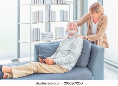 Happy Old Wife Take Care And Massage Shoulder Elderly Husband Sitting On Sofa In Living Room At Home. Lovely Senior Couple In Love Together On Couch