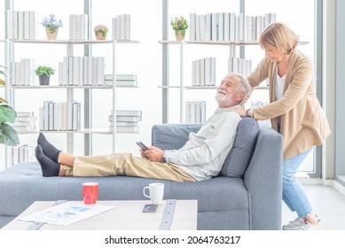 Happy Old Wife Take Care And Massage Shoulder Elderly Husband Sitting On Sofa In Living Room At Home . Lovely Senior Couple In Love Together On Couch