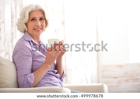 Happy old woman drinking beverage at home