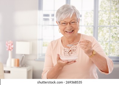 Happy Old Woman Eating Breakfast Cereal, Smiling, Looking At Camera.