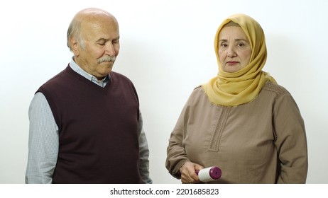 Happy Old Woman In Hijab Is Cleaning Pet Hair From Husband's Clothes With Sticky Clothing Roll.Studio Portrait Of Elderly Husband And Wife Isolated On White Background.Cat,dog And Pet Hair On Clothes.