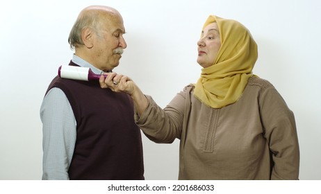 Happy Old Woman In Hijab Is Cleaning Pet Hair From Husband's Clothes With Sticky Clothing Roll.Studio Portrait Of Elderly Husband And Wife Isolated On White Background.Cat,dog And Pet Hair On Clothes.