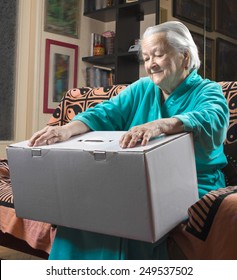 Happy Old Woman Holding A Large Cardboard Box At Home