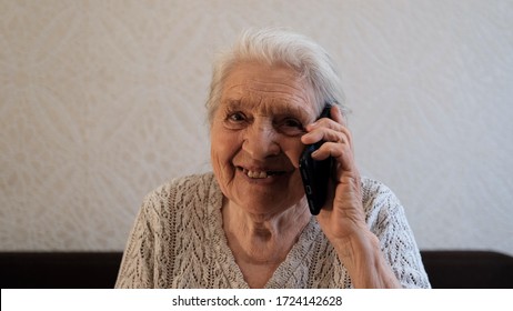 A happy old woman is talking on the phone and smiling.
