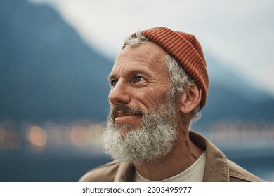 Happy older bearded man standing in nature park enjoying landscape. Smiling active mature traveler looking away exploring camping tourism nature mountains view feeling freedom. Close up portrait