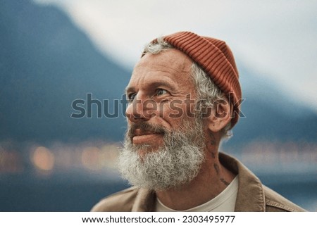 Happy older bearded man standing in nature park enjoying landscape. Smiling active mature traveler looking away exploring camping tourism nature mountains view feeling freedom. Close up portrait