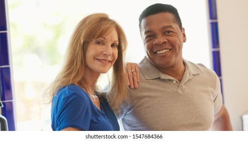 Happy Older Caucasian And African American Husband And Wife Standing In Their Kitchen Smiling. Senior Mixed Race Couple Homeowners Looking At Camera