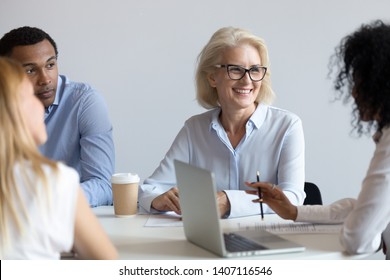 Happy Older Commercial Client Representative Discussing Deal With African Young Partner At Group Negotiation, Diverse Business People Workers Sitting At Office Table Talking At Team Corporate Meeting