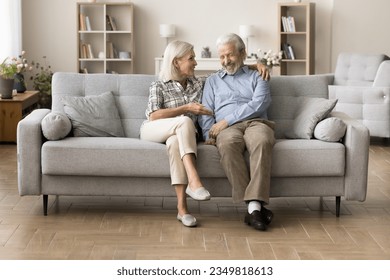 Happy older couple of grandparents enjoying leisure, conversation on home sofa together, talking, laughing, discussing retirement, elderly healthcare, family news, having fun. Full length shot - Powered by Shutterstock