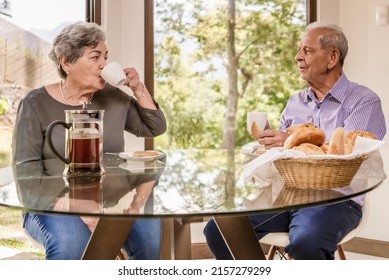 Happy older couple sitting in the dining room at home and talking. Senior man and woman relaxing drinking coffee.