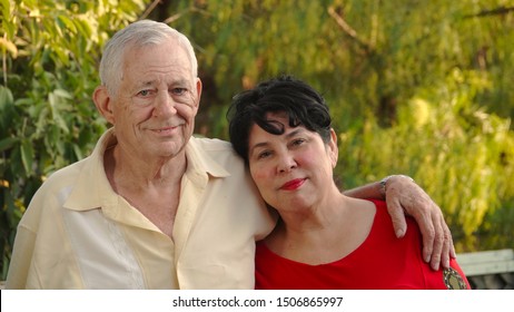 Happy, Older Couple Smiling. The Man (80 Year Old Caucasian) Has His Arm Around His Wife's Shoulder (62 Year Old Hispanic).                                