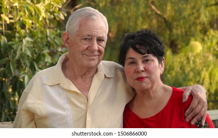 Happy, Older Couple Smiling. The Man (80 Year Old Caucasian) Has His Arm Around His Wife's Shoulder (62 Year Old Hispanic).                                