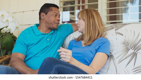 Happy Older Couple Talking On The Front Porch Of Their House. Smiling African American And Caucasian Husband And Wife Having Conversation Outside Their Home On A Sunny Day