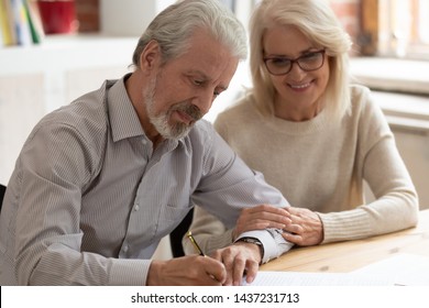 Happy older family couple husband and wife sign legal paper insurance contract write will testament, senior clients customers put signature on business document make financial deal take bank loan