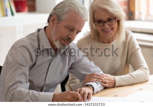 Happy older family couple husband and wife sign\
legal paper insurance contract write will testament, senior clients\
customers put signature on business document make financial deal\
take bank loan