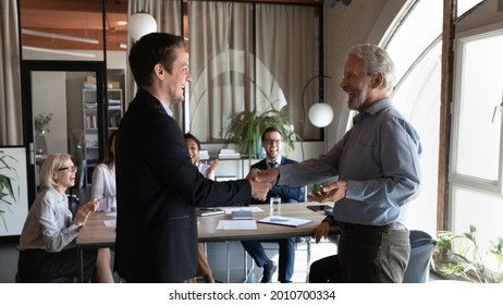 Happy Older Male Team Leader Giving Handshake To Excited Employee, Welcoming New Team Member, Congratulating On Good Work, Hiring For Job, Career Promotion. Team Clapping Hands And Laughing