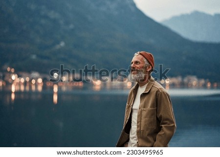 Happy older man standing in nature park enjoying natural park landscape. Smiling mature active traveler exploring camping tourism nature lake and mountains travel journey feeling freedom.