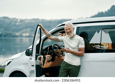 Happy older man standing near rv camper van on vacation using mobile phone. Smiling mature active traveler holding smartphone enjoying free roaming or internet in camping tourism nature park. - Powered by Shutterstock