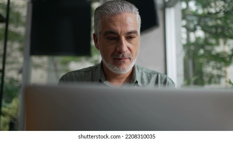 Happy Older Man Using Laptop Computer At Coffee Shop. Closeup Face Of A Senior Entrepreneur Looking At Screen Working Remotely At Cafe Place