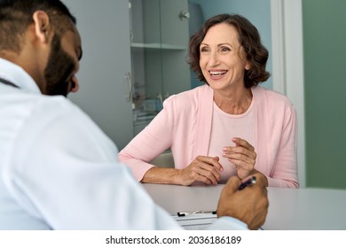 Happy Older Mature Female Patient Talking To Indian Male Doctor At Appointment. Healthy Smiling Senior Old Woman Feeling Cheerful About Good News At Medical Consultation. Elderly Health Medical Care.