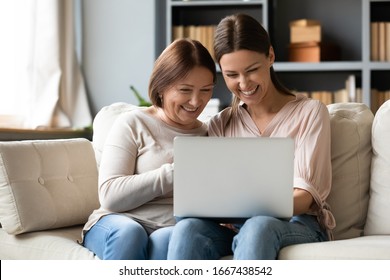 Happy older mature mother sitting on sofa with excited grownup daughter, looking at laptop screen. Laughing young woman showing funny video photos to elderly mommy, having fun together at home. - Powered by Shutterstock