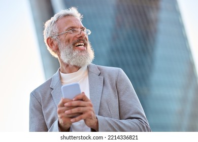 Happy older mature stylish professional business man, smiling senior 60 years old businessman wearing suit holding smartphone using mobile cell phone tech standing outdoor in big city office district. - Powered by Shutterstock