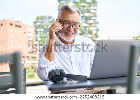 Happy older professional business man, smiling senior old businessman seller, merchant or entrepreneur holding mobile phone talking on cellphone making business call on cell standing in city outside.