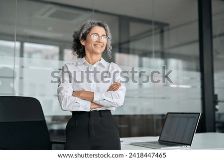 Happy older professional business woman standing in office looking away. Smiling middle aged mature business leader, senior female corporate manager, confident lady executive thinking of success.