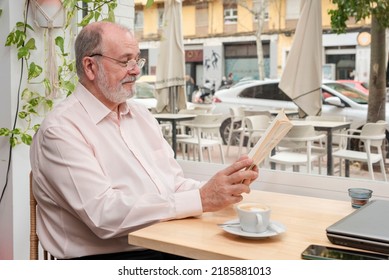 A Happy Older Retired Man Enjoying Reading A Book Sitting In A Coffee Shop While Drinks His Coffee