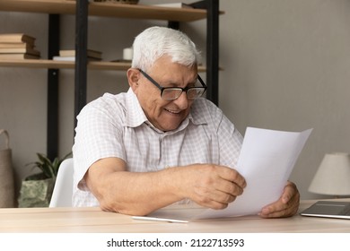 Happy Older Senior Landlord Man In Glasses Reviewing Document, Smiling, Laughing, Receiving Insurance Notification, Getting Letter With Good News, Doing Paperwork At Home, Paying Paper Bill, Fees