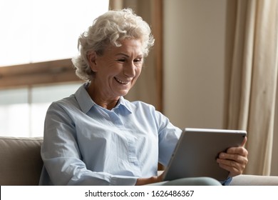 Happy Older Woman Holding Digital Tablet, Reading Electronic Book Alone At Home. Smiling Middle Aged User Web Surfing, Searching Information, Shopping Online In Internet Store, Chatting With Friends.