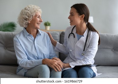 Happy Older Woman Talking With Friendly Doctor During Visit, Sitting On Couch, Receiving Good Medical Checkup Results, Physician Wearing White Uniform With Stethoscope Supporting Mature Patient