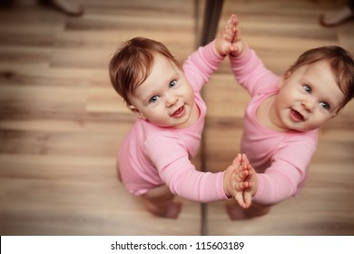 Happy One Year Old Baby Girl Looking Up Next To Mirror.