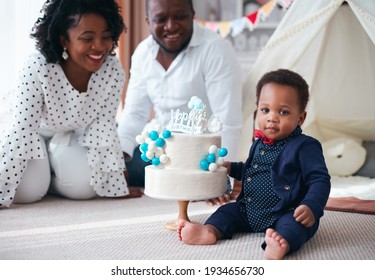 Happy One Year Old Baby Boy With Birthday Cake And Happy Parent On The Background