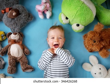 Happy one year old boy lying with many plush toys on blue blanket - Powered by Shutterstock