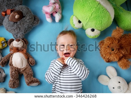 Happy one year old boy lying with many plush toys on blue blanket