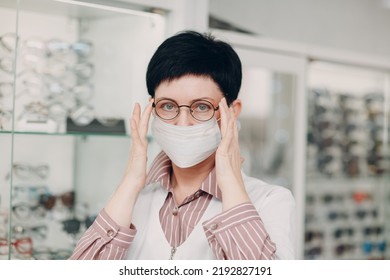 Happy Optician In Medical Face Mask Choosing Eyeglasses, Female Optometrist With Glasses.