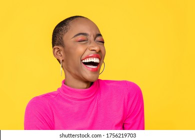 Happy optimistische Afroamerikanerin in bunten rosafarbenen Kleider, die einzeln auf gelbem Hintergrund lacht