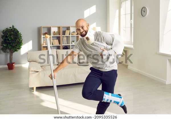 Happy optimistic man with multiple physical injuries\
after car crash accident standing in living room, leaning on\
crutch, smiling and giving thumbs up to show how much he\'s enjoying\
sick leave at home