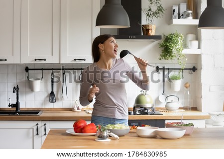 Happy optimistic millennial Caucasian woman have fun singing dancing in modern kitchen cooking in morning, overjoyed funny young woman enjoy lazy leisure weekend at home while preparing food