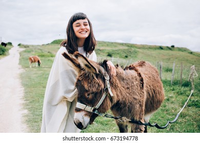 Happy and optimistic woman unites with nature by caressing funny cute donkey, hugs him and laughs into camera - Powered by Shutterstock