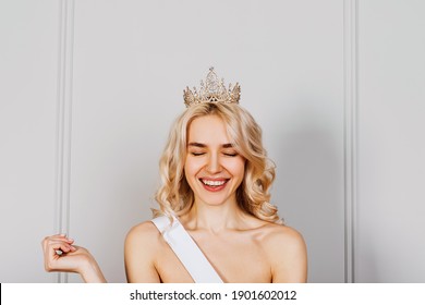 Happy Oung Blonde Woman Wearing A Diamond Golden Crown And A White Ribbon, With Eyes Closed, Smiling. Beauty Contest Winner Concept.