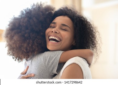 Happy Overjoyed African American Single Mother Hugging Cute Little Kid Daughter And Laughing, Cheerful Loving Black Mom Embracing Child Girl Having Fun Playing Cuddling Bonding Feeling Joy Affection