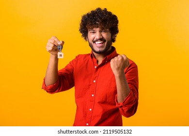 Happy overjoyed guy holding the keys with keychain in form of little house isolated on orange background. Smiling indian man holding keys from new property, happy buyer of own estate. Guy relocated