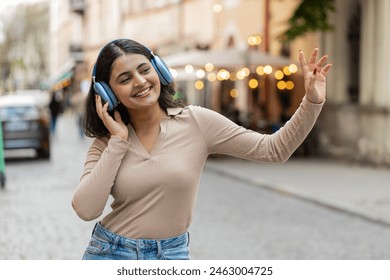 Happy overjoyed Indian young woman in wireless headphones dancing listening favorite energetic disco music in smartphone dancing outdoors. Hispanic girl walking on urban city street. Town lifestyles - Powered by Shutterstock