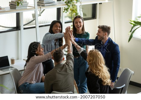 Happy overjoyed mixed race millennial team celebrating success, work achieve, giving high five, shouting, smiling, laughing. Teammates excited with great group result, keeping high motivation