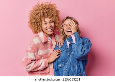 Happy overjoyed young women laugh gladfully hear something very funny dressed in fashionable clothes stand closely to each other isolated over pink background. Friendship and emotions concept